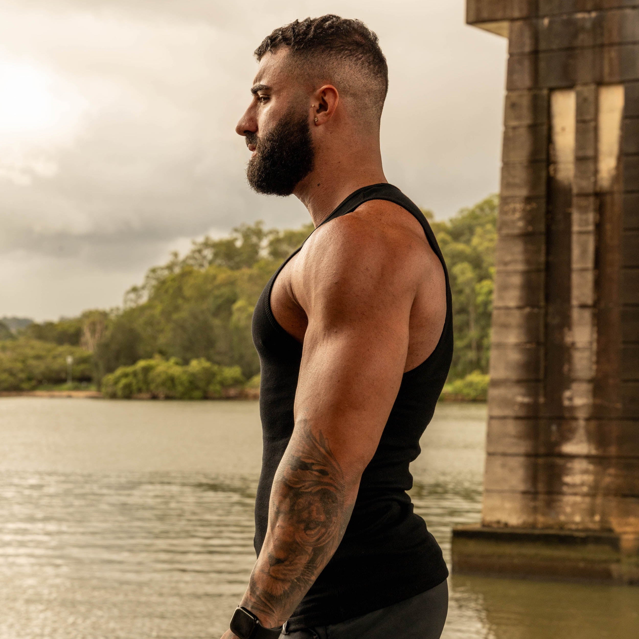 side pose showing muscular physique in LionBuilt black tank top by water