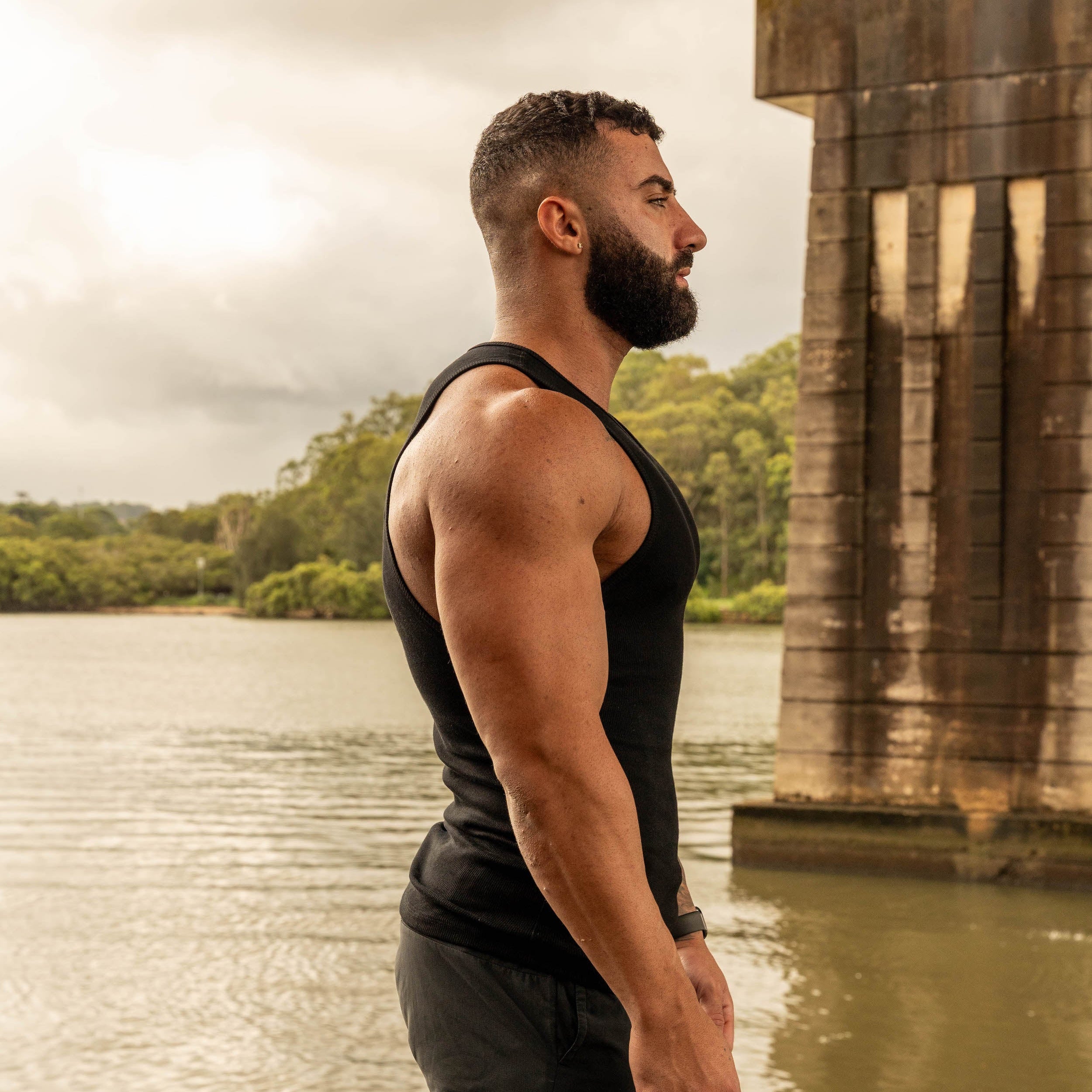 side pose showing muscular physique in LionBuilt black tank top by water