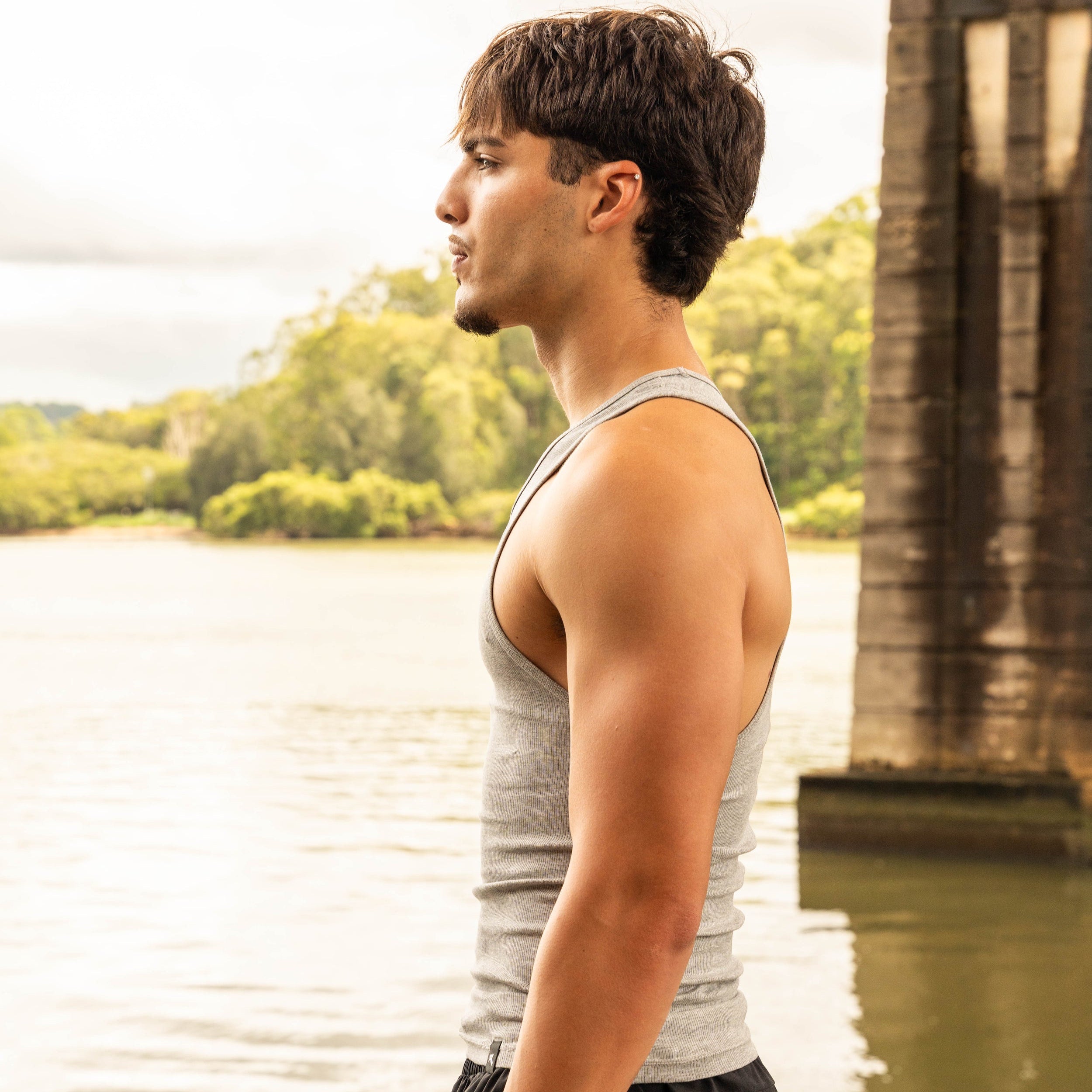 side pose showing muscular physique in LionBuilt black tank top by water