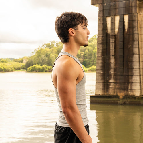side pose showing muscular physique in LionBuilt black tank top by water