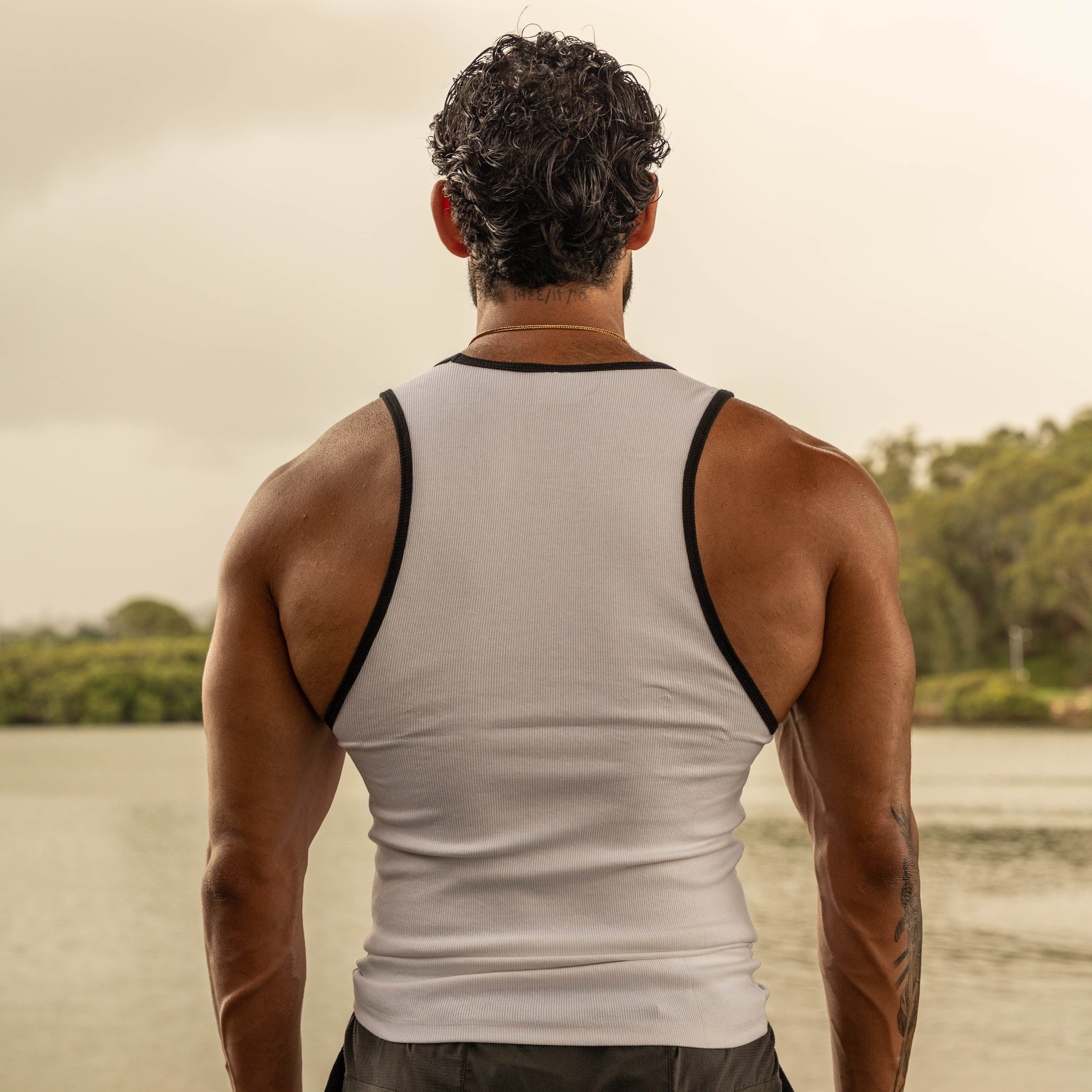 back pose showing muscular physique in LionBuilt white tank top by water