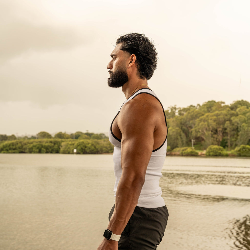 side pose showing muscular physique in LionBuilt white tank top by water