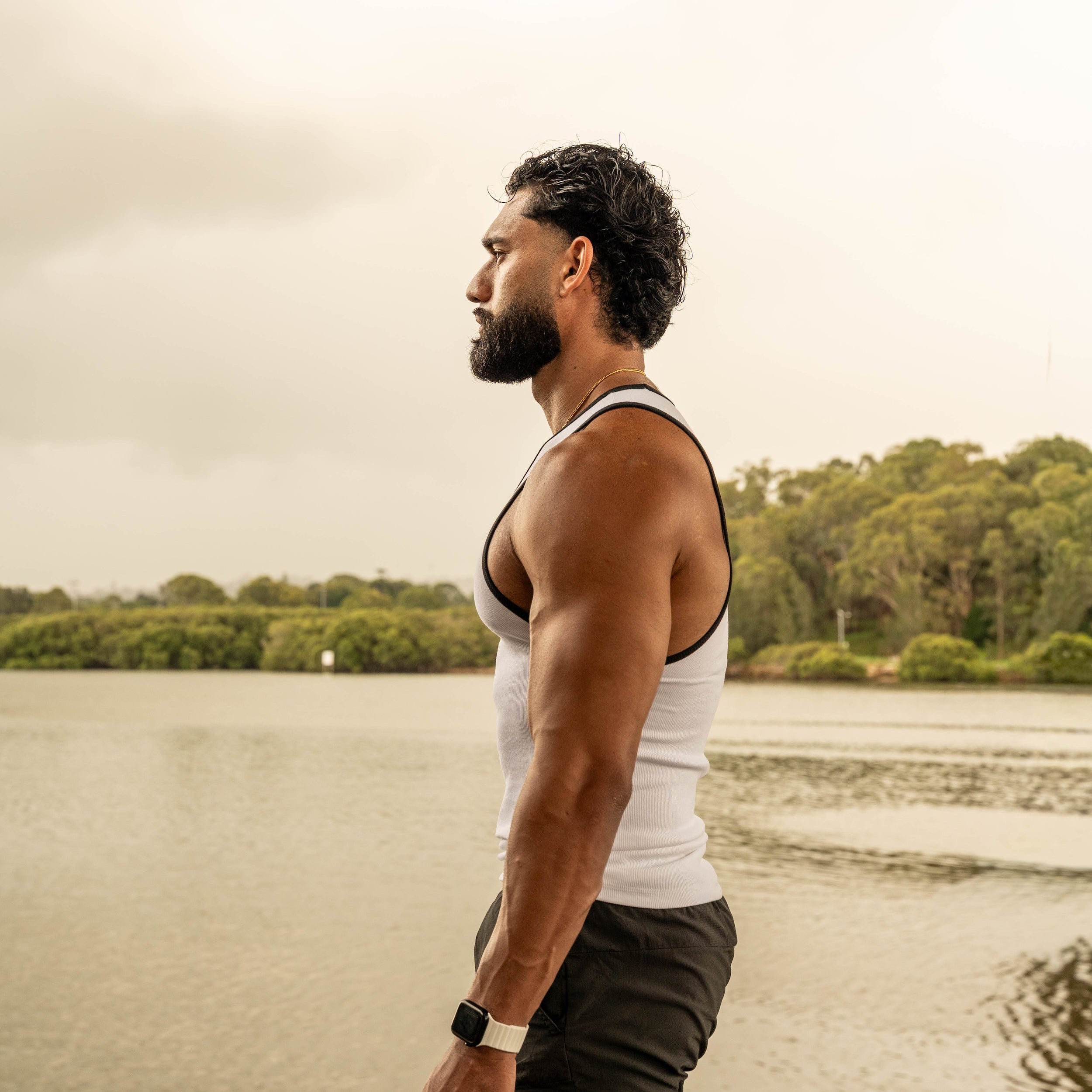 side pose showing muscular physique in LionBuilt white tank top by water