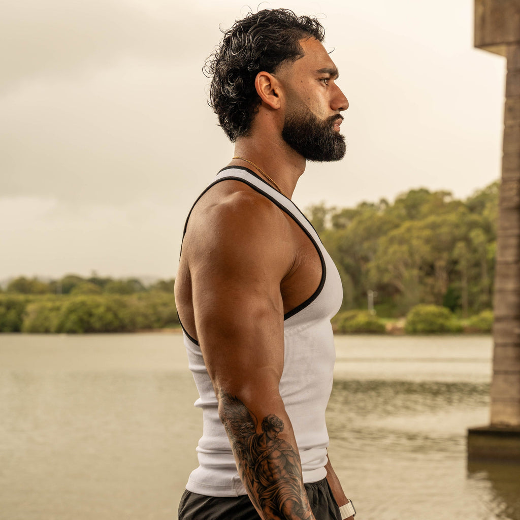 side pose showing muscular physique in LionBuilt white tank top by water